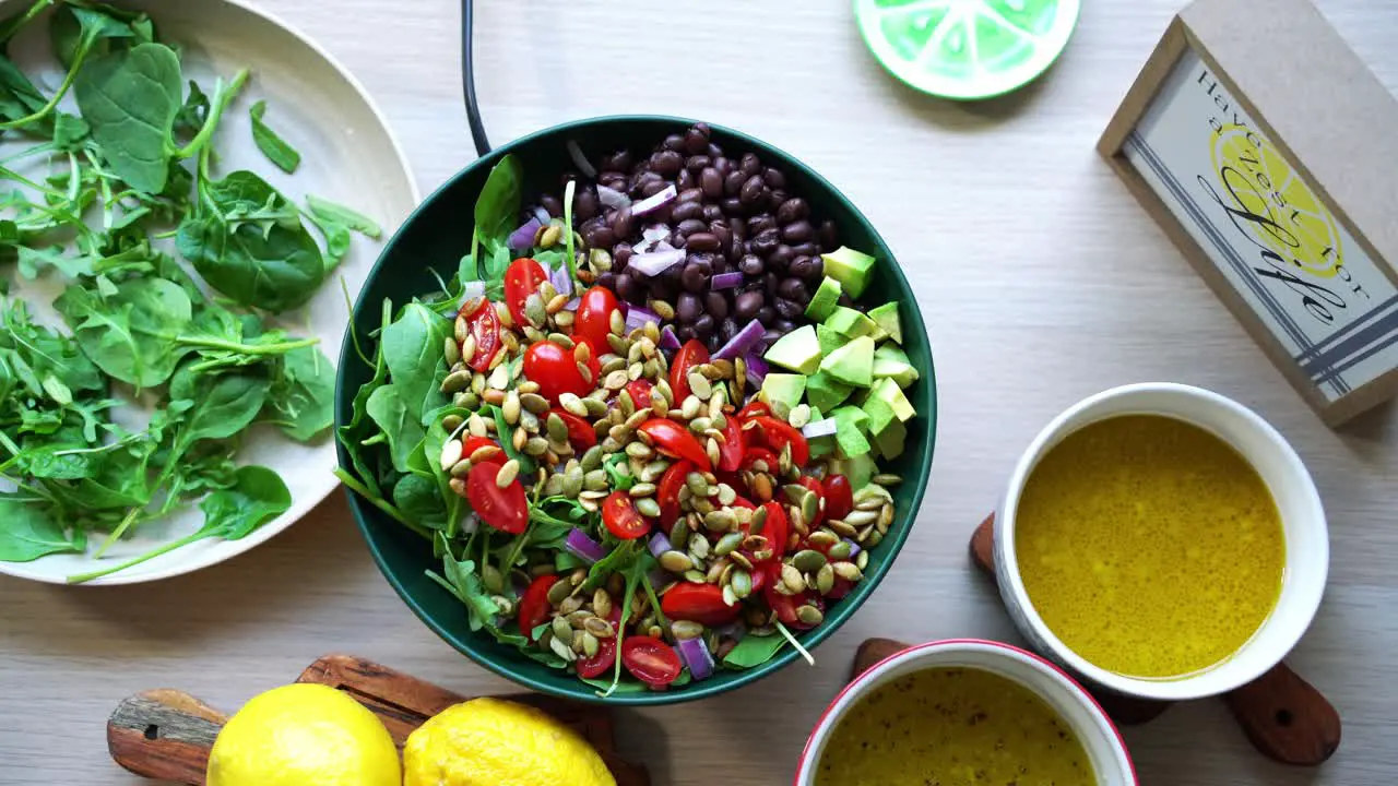 Top view aerial shot of salad on platform black beans lemons pumpkin seeds avocado tomatoes leaf spinach dressing