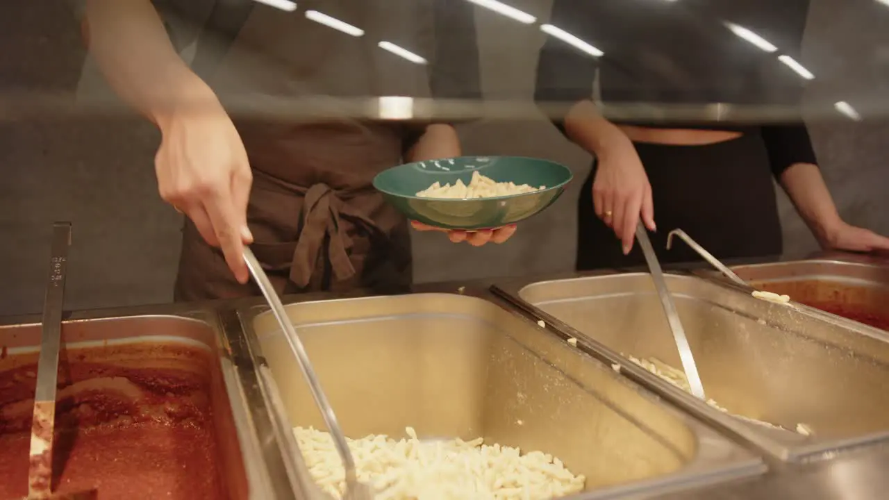 someone from the catering puts noodles and then sauce on a plate and gives it to the buyer