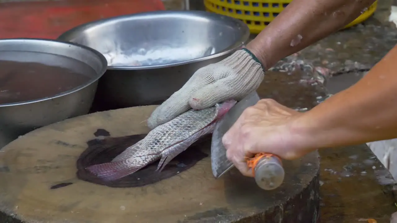 filleting tilapia fish with a chop knife in street market