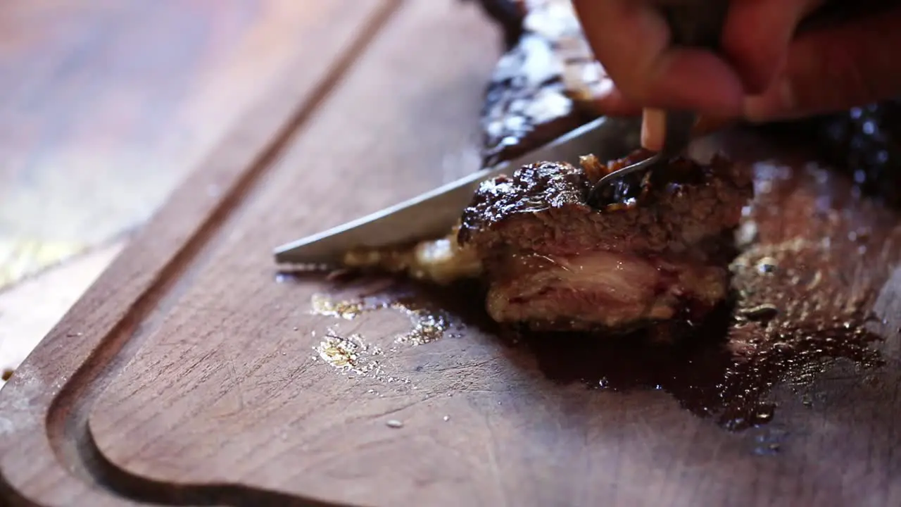 Close up view of Male hand with a knife slicing a piece of meat on cutting Board