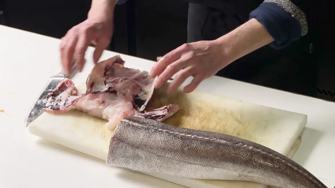 Chef tearing apart peaces of fish from a hake's head while cleaning it up in a Spanish restaurant in Madrid