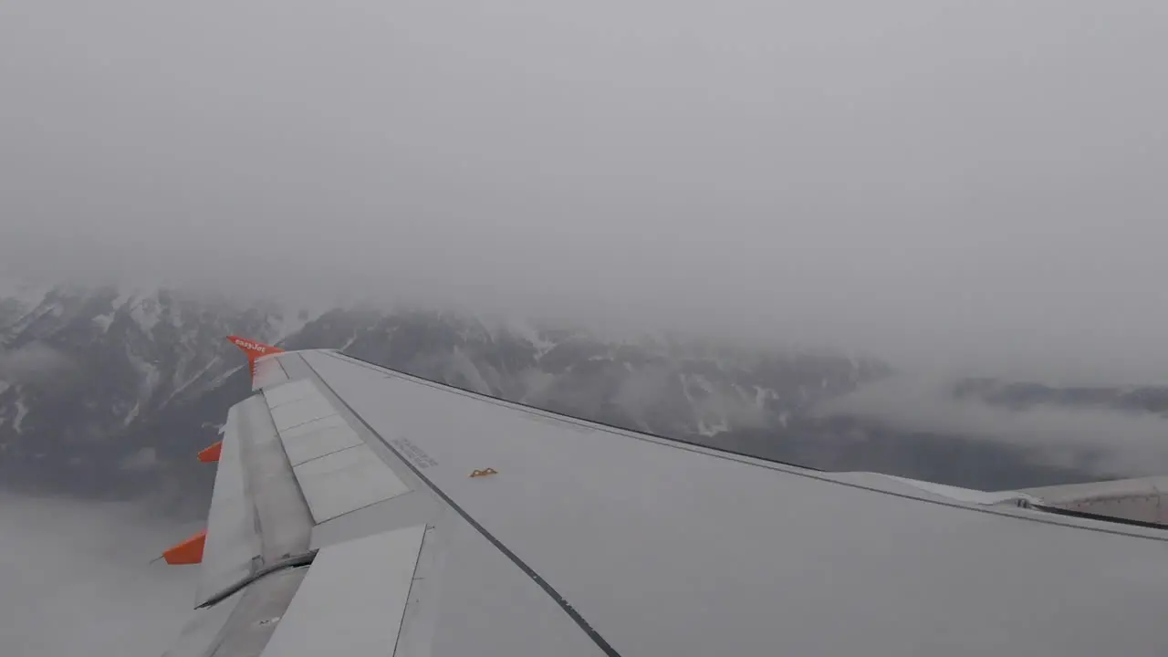 Plane wing as plane takes off flying over cloudy snowy mountains in Austria