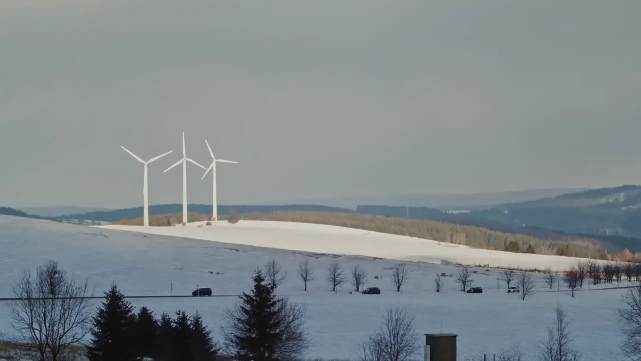 Three windmills in snow white landscape cars passing on road Klinovec Czech Republic