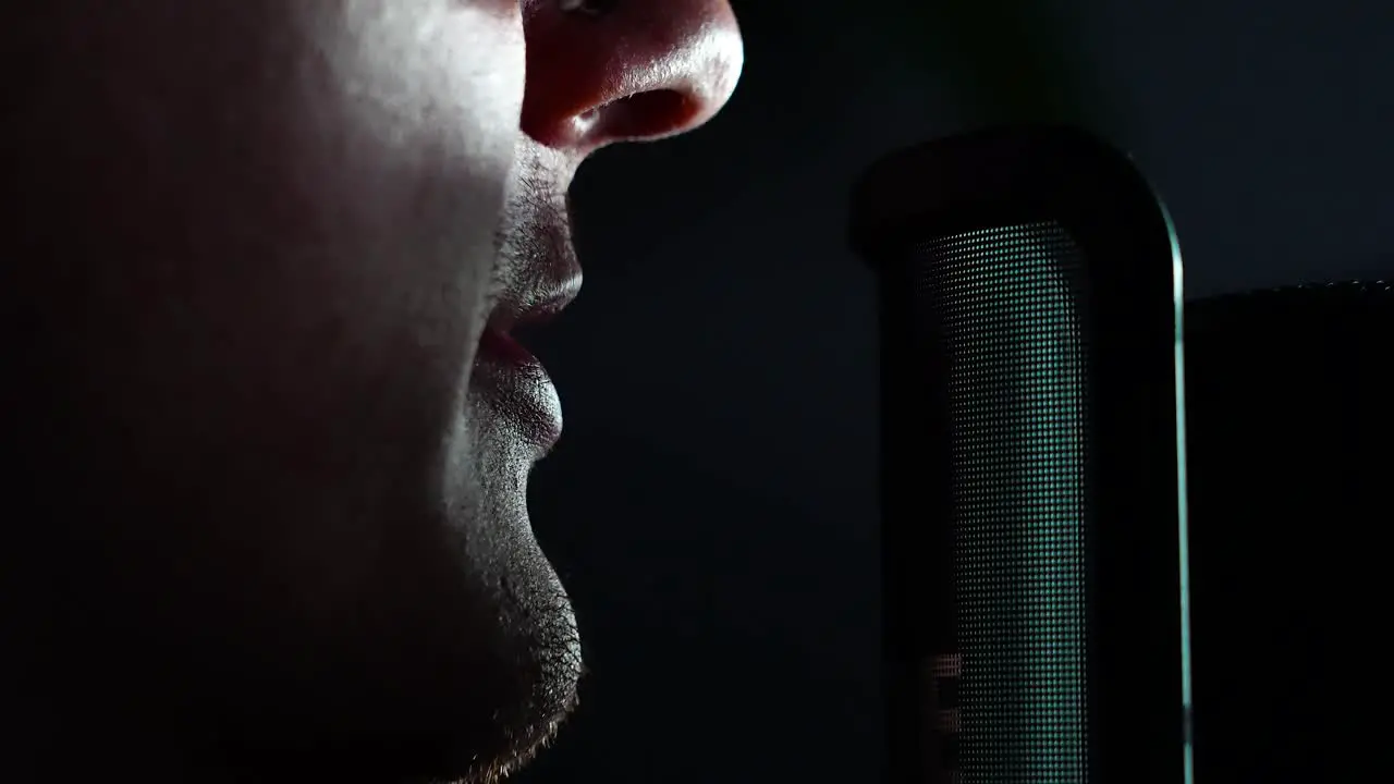 Man talking into a microphone front of computer streamer speaking into mic dark room static shot