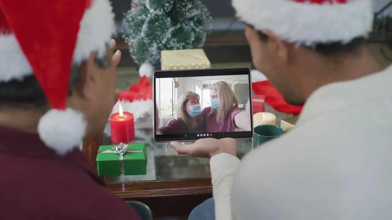 Biracial father and son waving and using tablet for christmas video call with happy family on screen