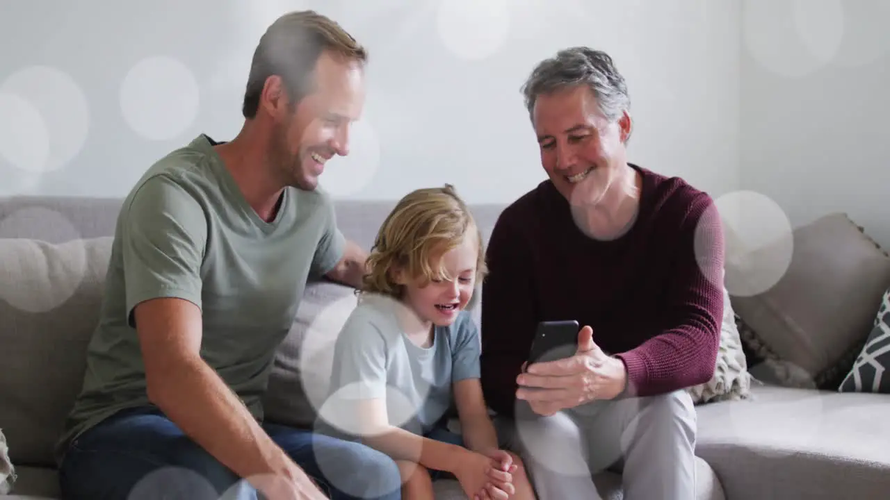 Animation of bokeh over happy grandfather father and son on sofa