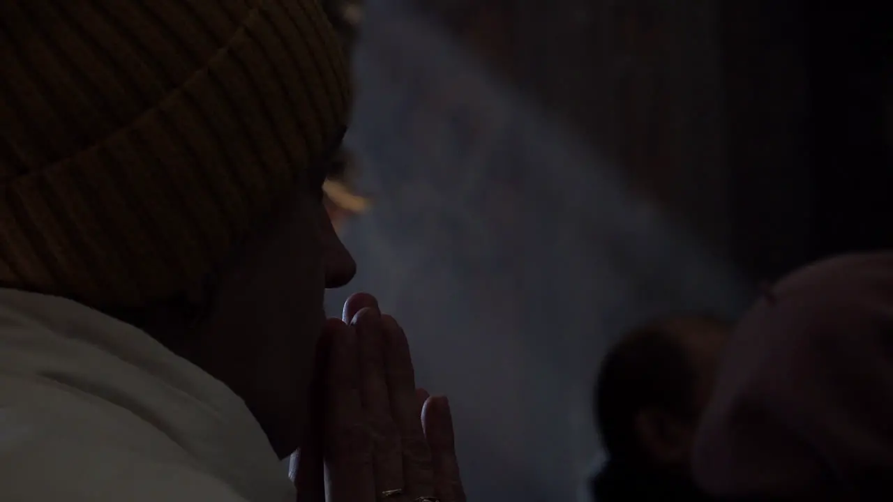 A woman puts her hands together in prayer as light pours through a window at the funeral of a Ukrainian soldier during the Russian invasion of the country