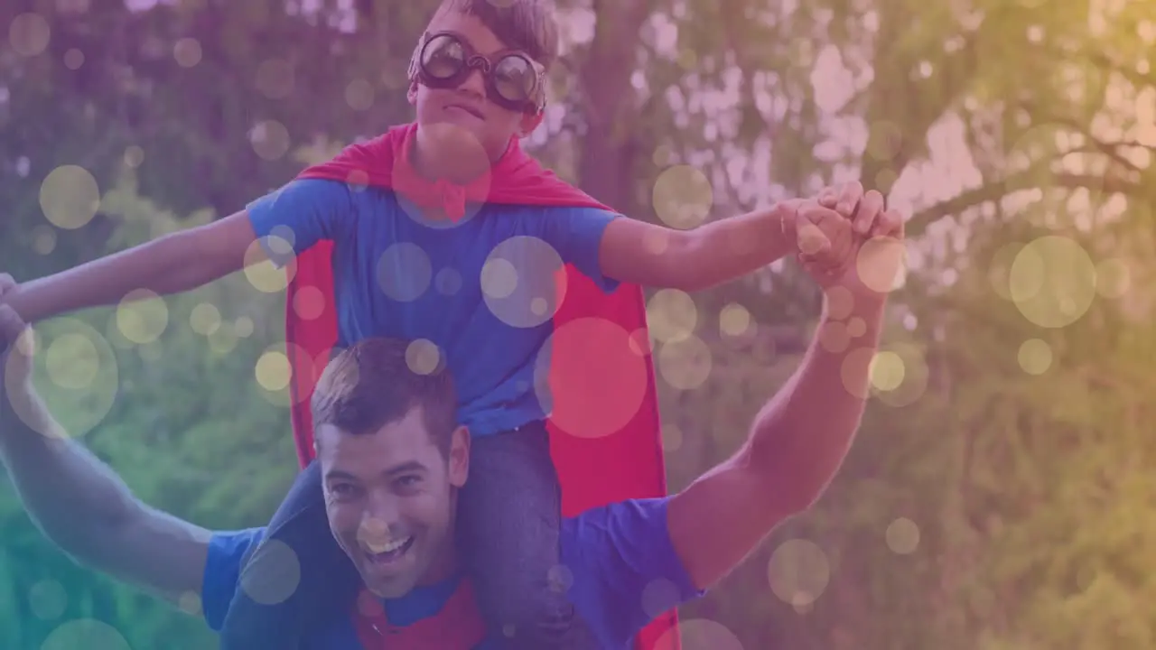 Animation of bokeh over happy caucasian father and son in superhero costumes