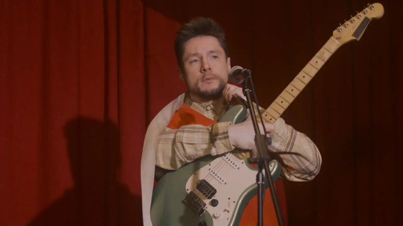 Concentrated Male Musician With Guitar And Microphone Sitting On Stool And Getting Ready For A Live Performance