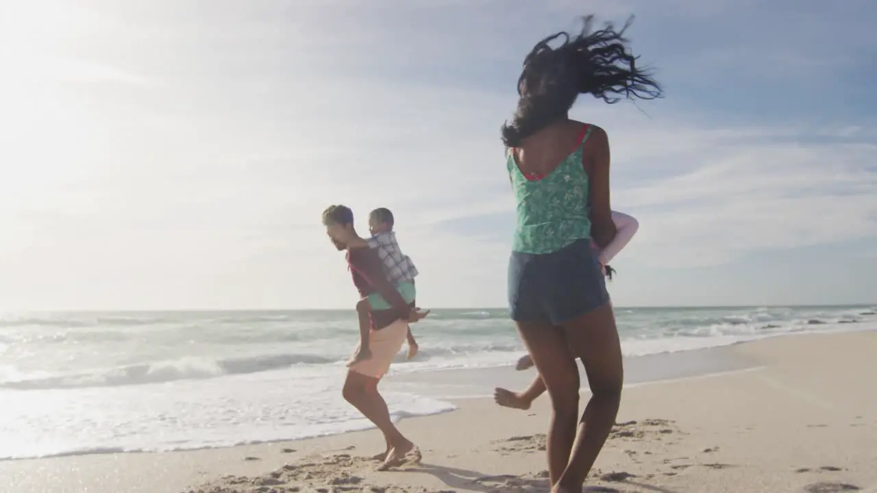 Happy hispanic parents playing with children on beach in sun