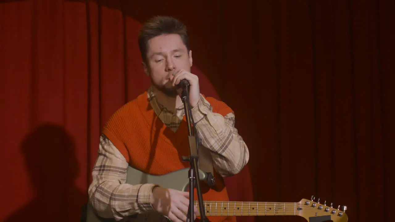 Concentrated Male Musician With Guitar And Microphone Sitting On Stool And Getting Ready For A Live Performance 1