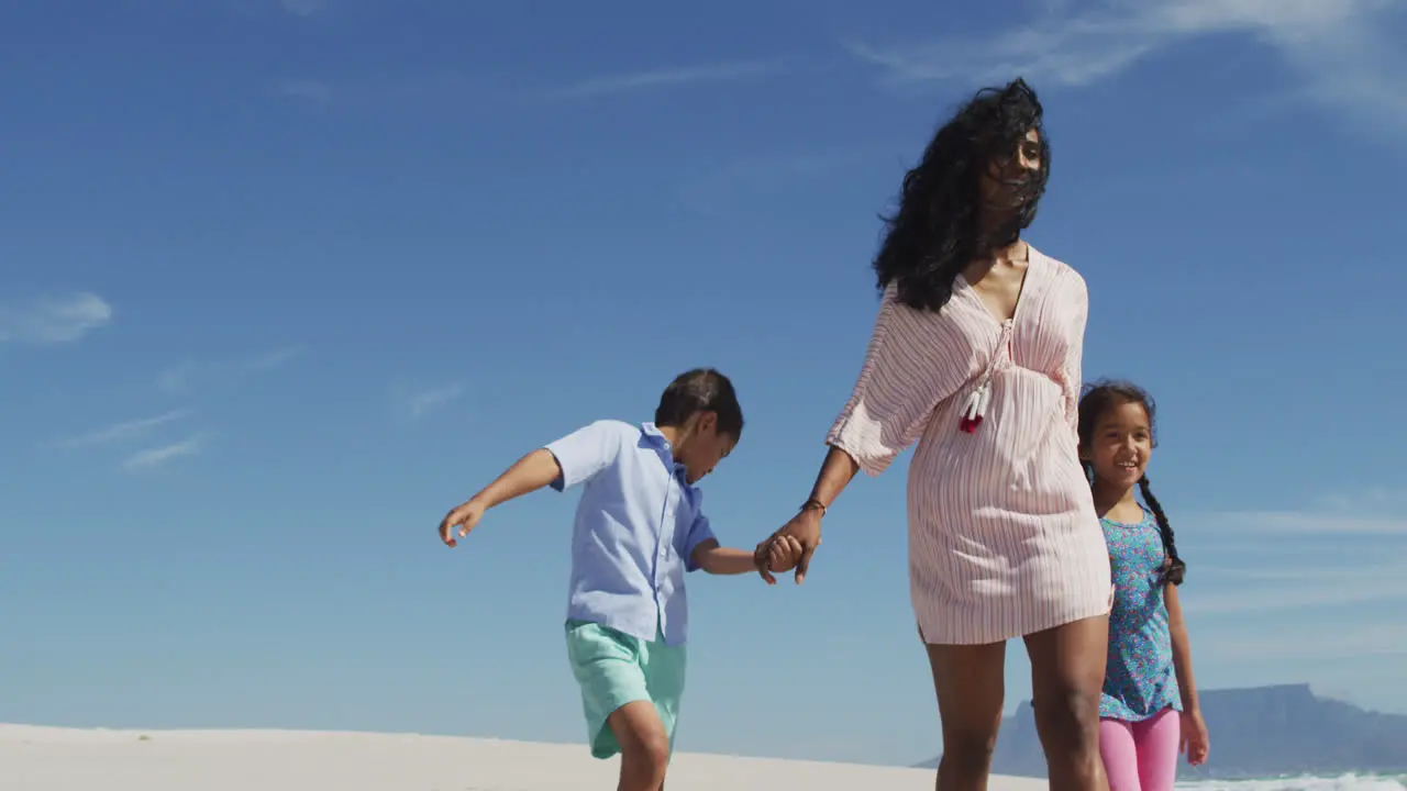 Happy hispanic mother walking with daughter and son on beach