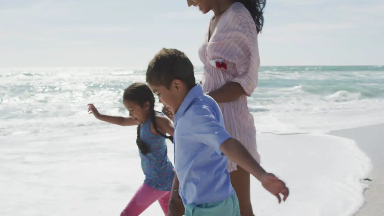 Midsection of happy hispanic moter with daughter and son walking on beach