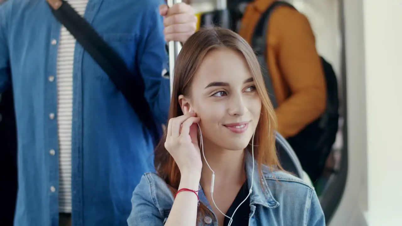 Close Up Of The Young Attractive Happy Girl Putting Headphones In Ears And Listening To The Music On The Smartphone While Going In The Tram