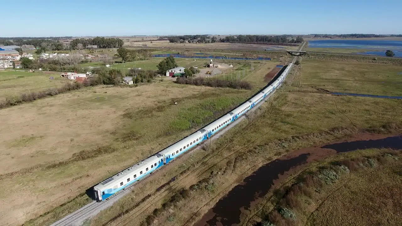 long passenger train traveling through countryside blue and white cars near Buenos Aires