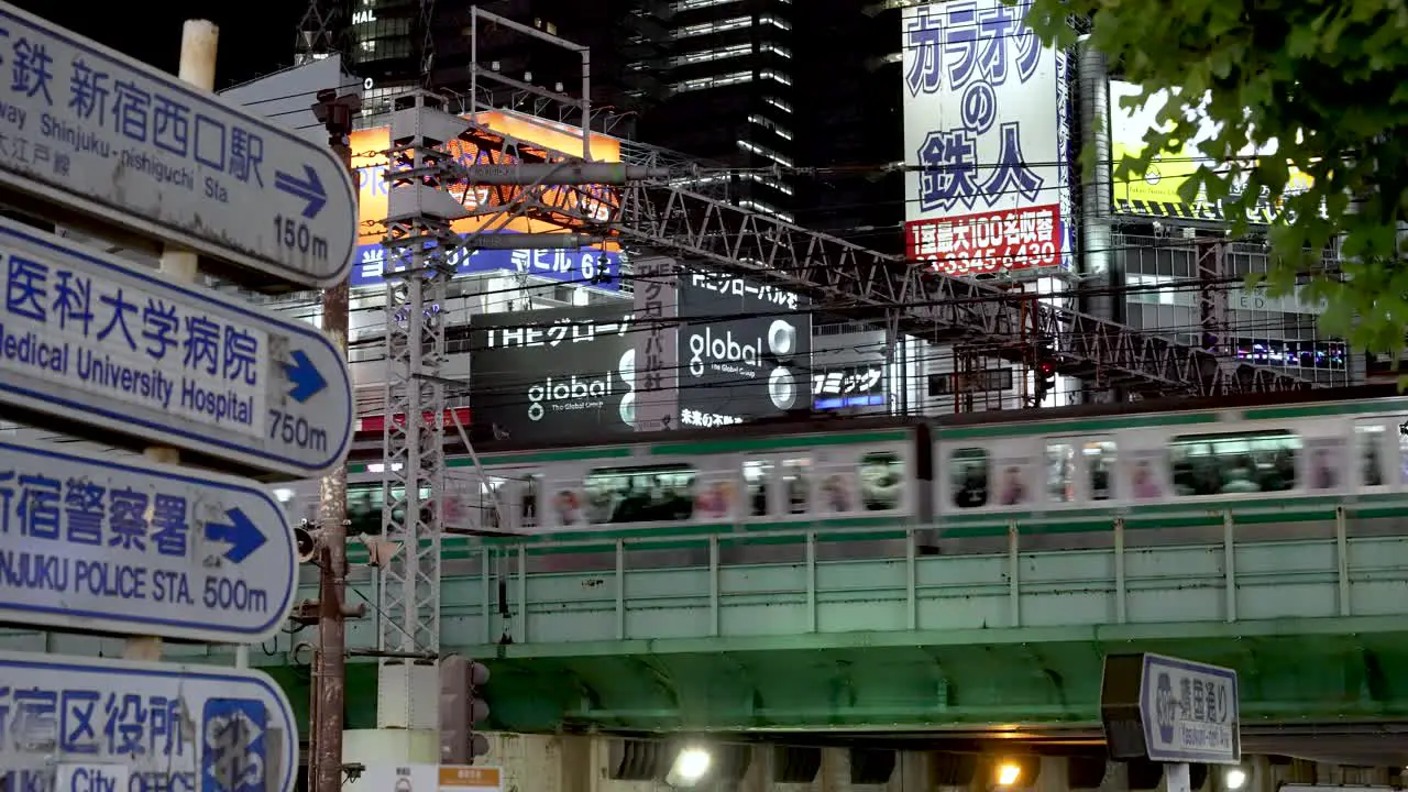 Yamanote Line Train Passing On Elevated Train Track In Shinjuku At Night With View Of Information Road Signs In View