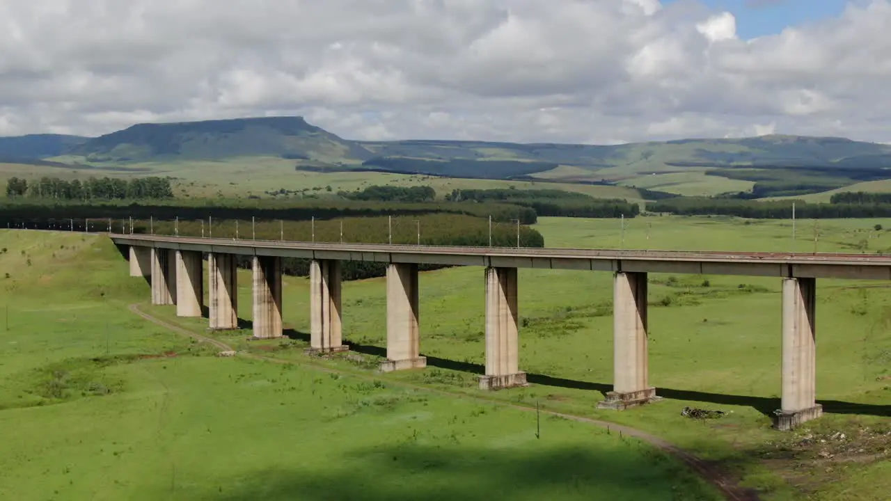 Aerial orbit left of railway overpass in lush green meadows and pine forests