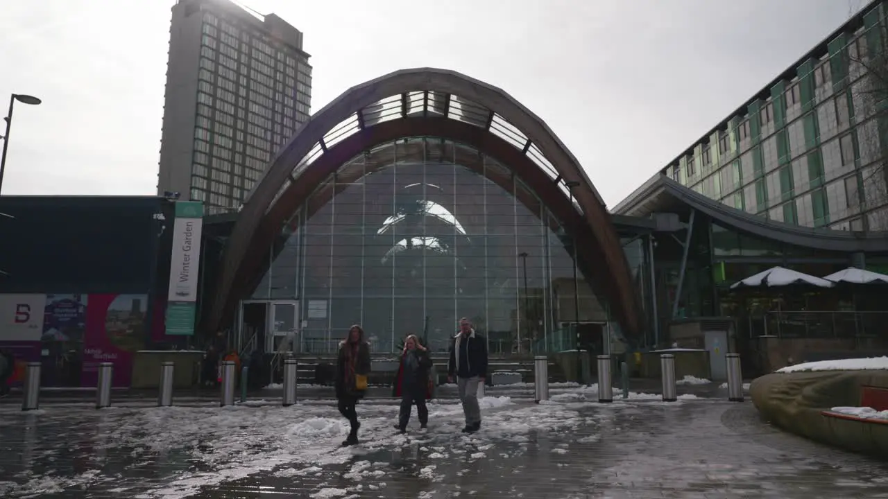 People walking in the street past the Winter Garden attraction in Sheffield city centre during snowy winter time