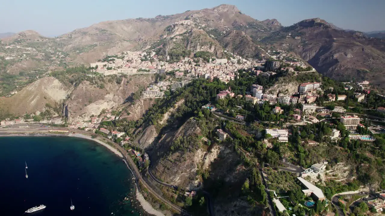 Drone flying over the ocean towards a city built on top of the mountain called Taormina