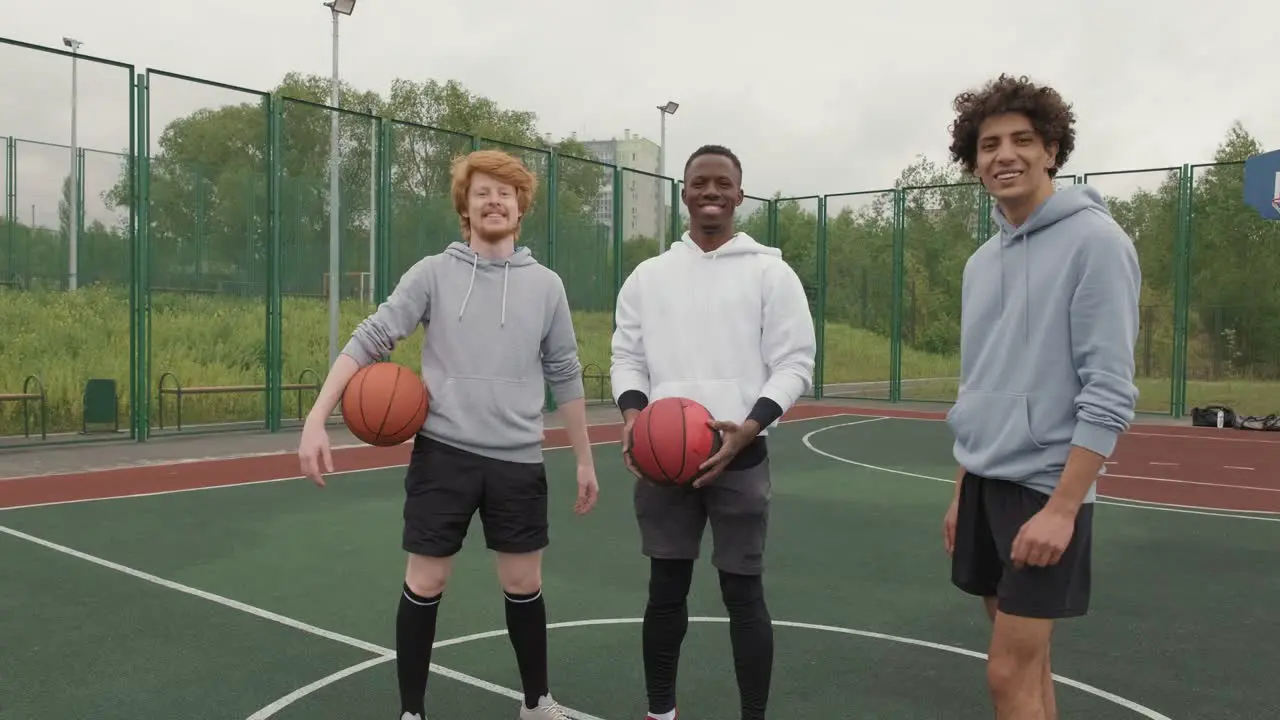 Three Friends With Basketballs On Basketball Court Smiling And Looking At Camera