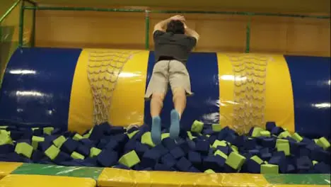 Backside footage in slow-motion of a male jumping into apool with plush cubes