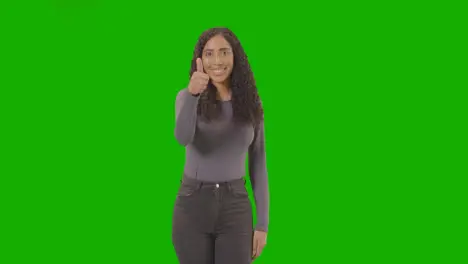 Studio Three Quarter Length Shot Of Woman Giving Thumbs Up Sign Against Green Screen