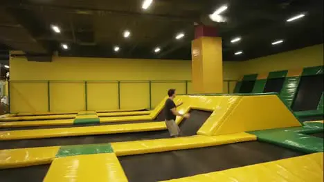 Young male athlete training on professional trampoline Practicing frontal somersaults springing over barriers