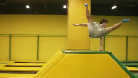 Male gymnast trains on professional trampoline springs over the barrier with the body twist and following back somersault