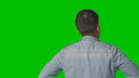 Studio Rear View Of Casually Dressed Young Man Looking At Green Screen 