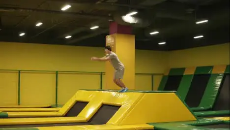 Young male athlete in beige t-shirt and shorts jumps on trampoline and enjoys doing front double somersaults Youth sport gymnastics