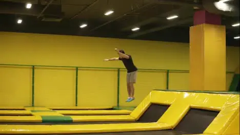 Young attractive sportive athlete performs front somersaults and body twistsat professional trampoline for training