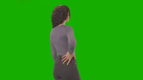 Rear Three Quarter Length Studio Shot Woman Standing Against Green Screen With Hand On Hips