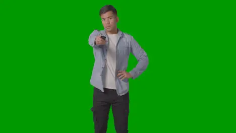 Studio Shot Of Casually Dressed Young Man With Remote Control Flicking Through TV Channels Against Green Screen 2