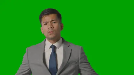 Portrait Of Frustrated Businessman In Suit Against Green Screen Talking To Camera