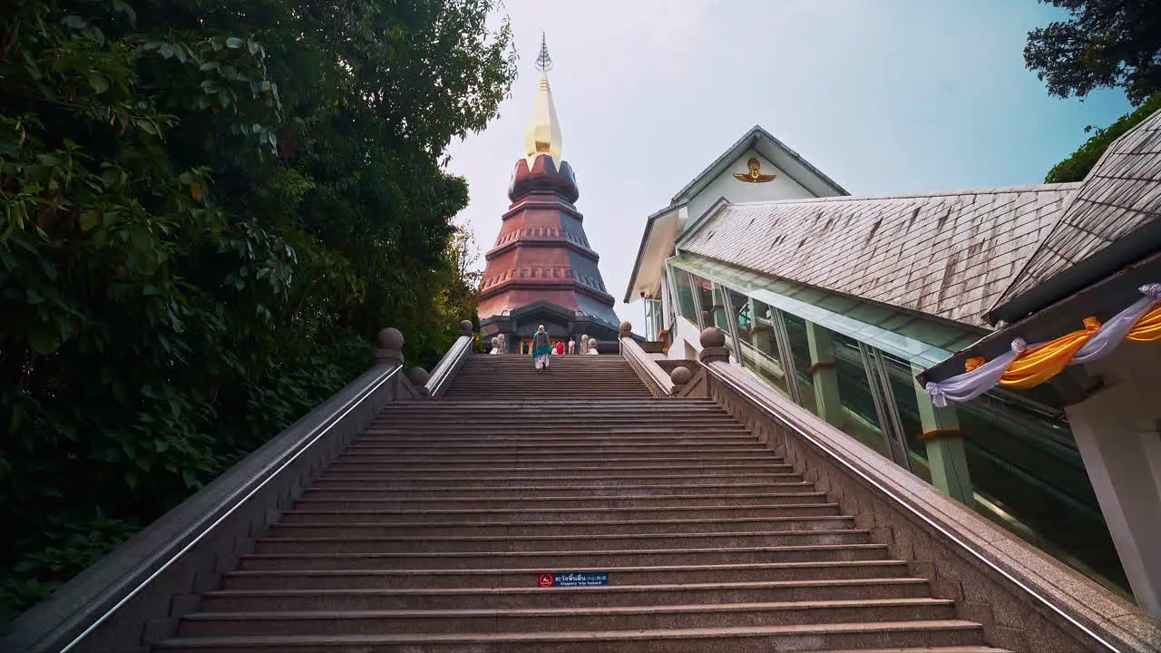 Woman in poncho climbing up long stairway leading to pagoda Thailand