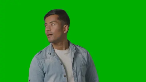 Portrait Of Casually Dressed Smiling Young Man Looking Around Against Green Screen 