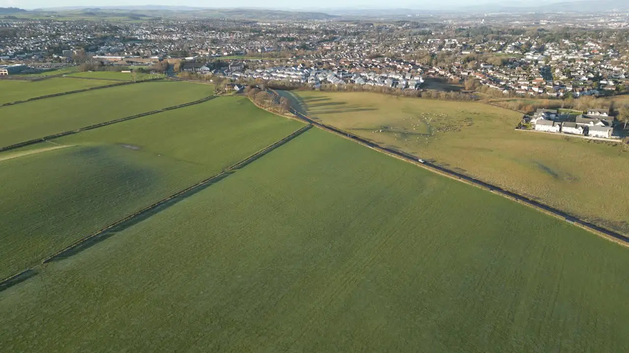 Aerial view of a green field with a road and a great city in the background