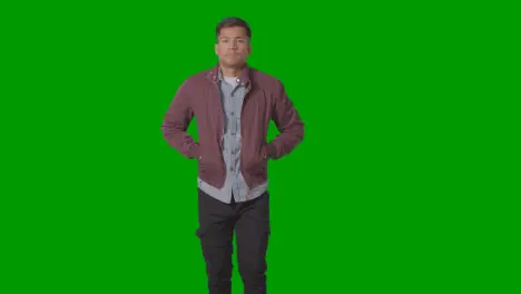 Portrait Of Casually Dressed Smiling Young Man Putting Hands In Jacket Lockets Against Green Screen 