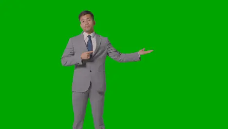 Three Quarter Length Shot Of Businessman In Suit Presenting Or Showing Against Green Screen 