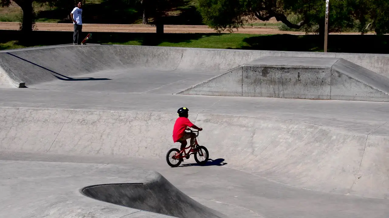 Older skater watches boy ride bike in the park