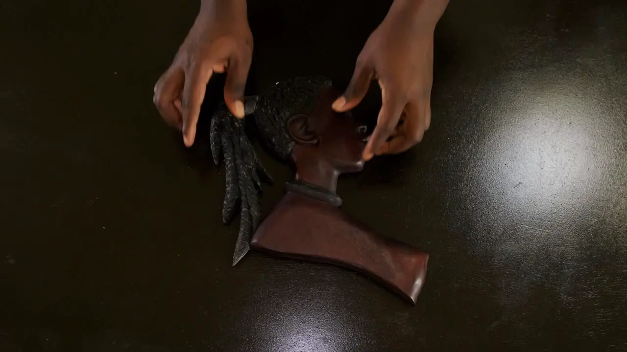 Top down shot of an African American man's hands placing a female wooden African mask on a brown table