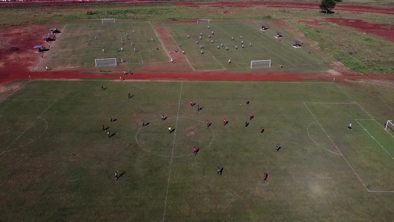 Drone fly over football matches being played on three football fields one in foreground and two in the background