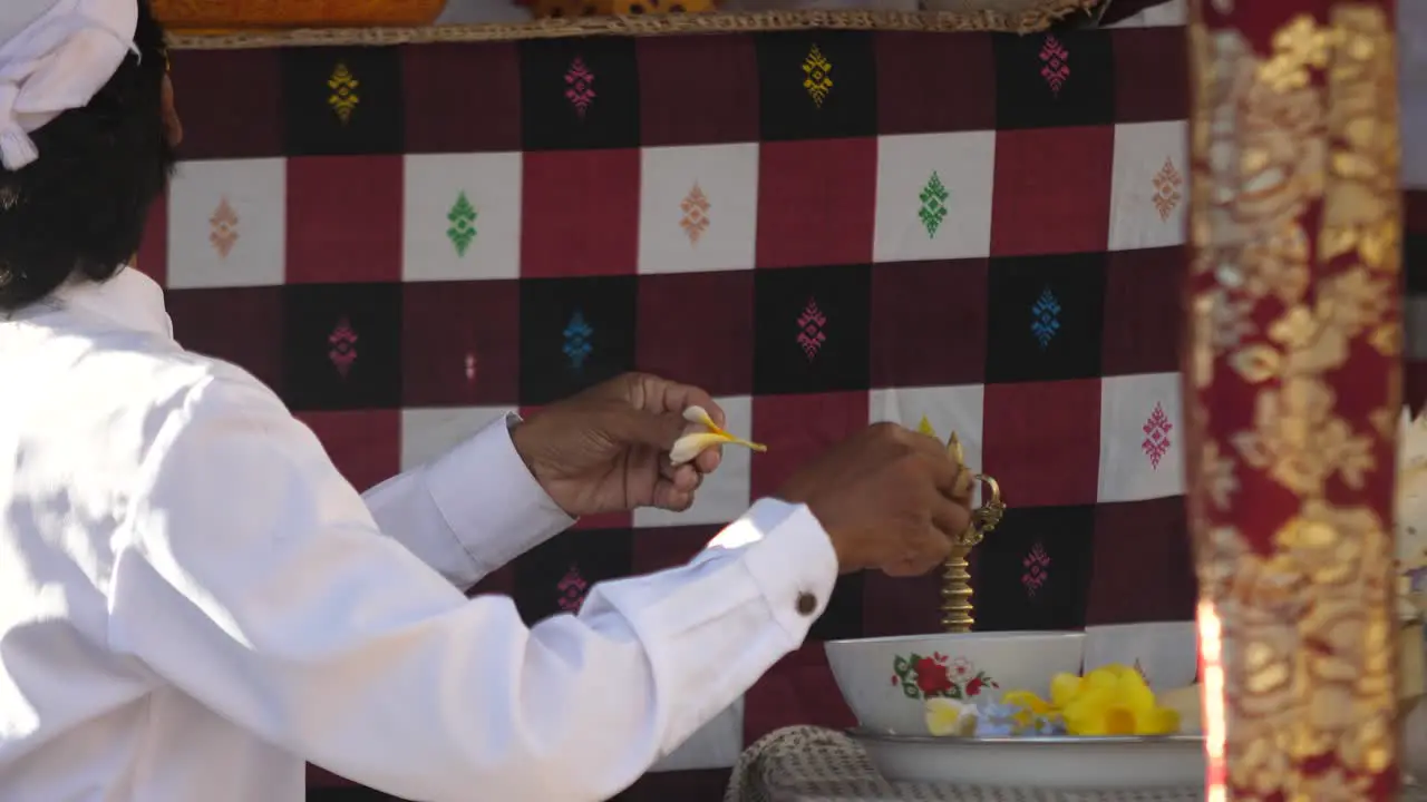 Hindu priest prepares an offering with bright yellow flowers at an altar in a temple of Bali Indonesia