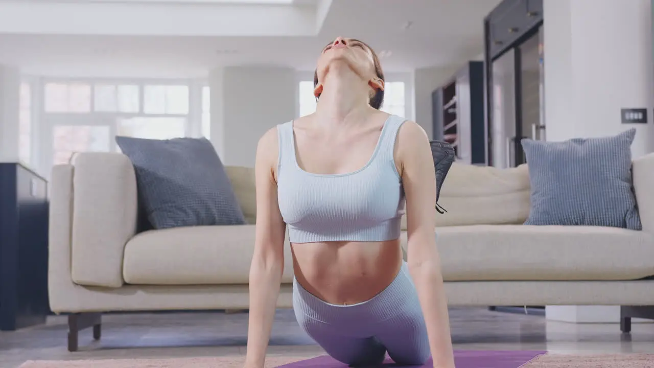 Woman in fitness clothing at home in lounge doing stretches and exercising on mat- shot in slow motion