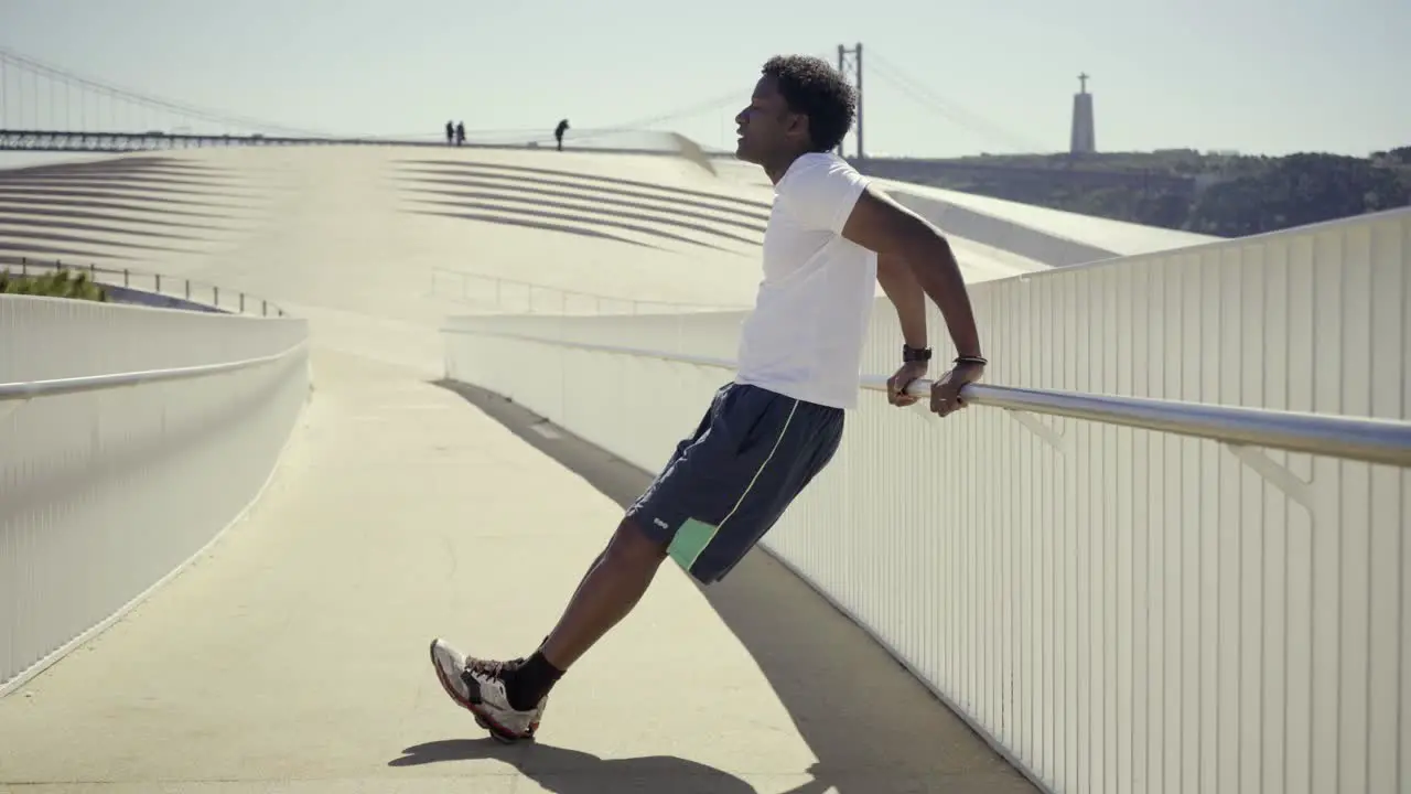 Side view of sporty young man doing push-ups near metal railing