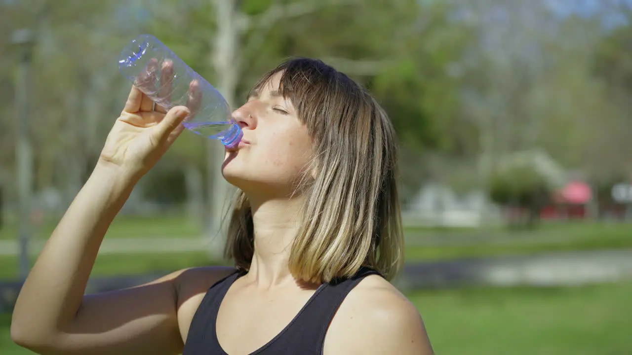 Beautiful young woman drinking water from plastic bottle