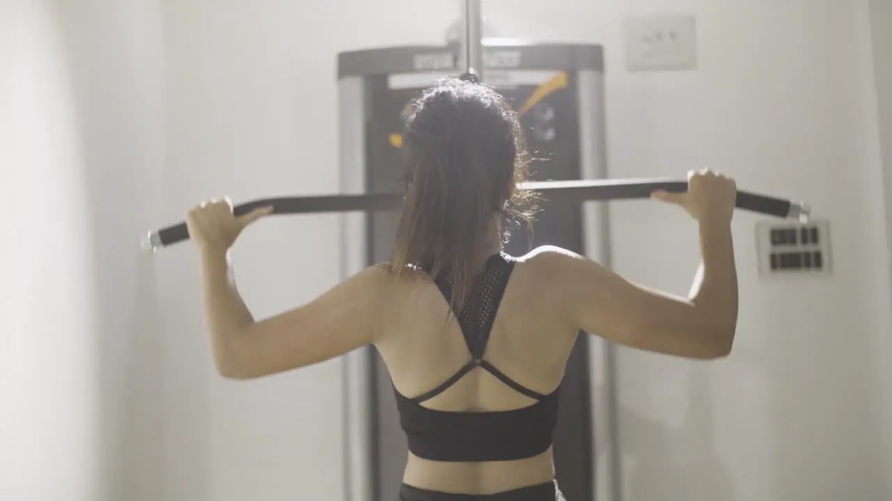 Backside of fitness girl working out at gym using lat pulldown equipment or machine slow motion