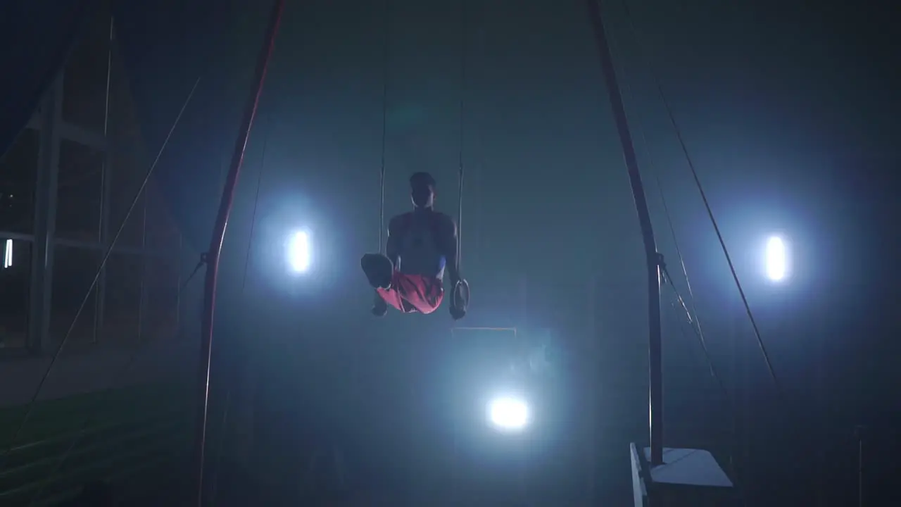 male gymnast athlete performs handstand and rotation on rings on dark background and smoke in slow motion