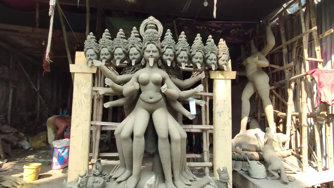 Unfinished clay idols of Indian goddess at workshop people working behind smooth camera movement