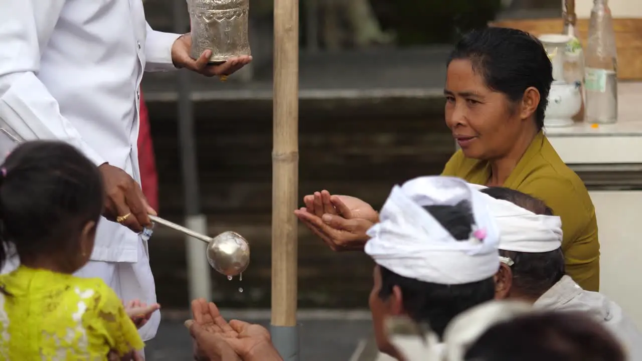 Balinese followers of Hinduism receive holy water from priest poured into cupped hands and take a sip